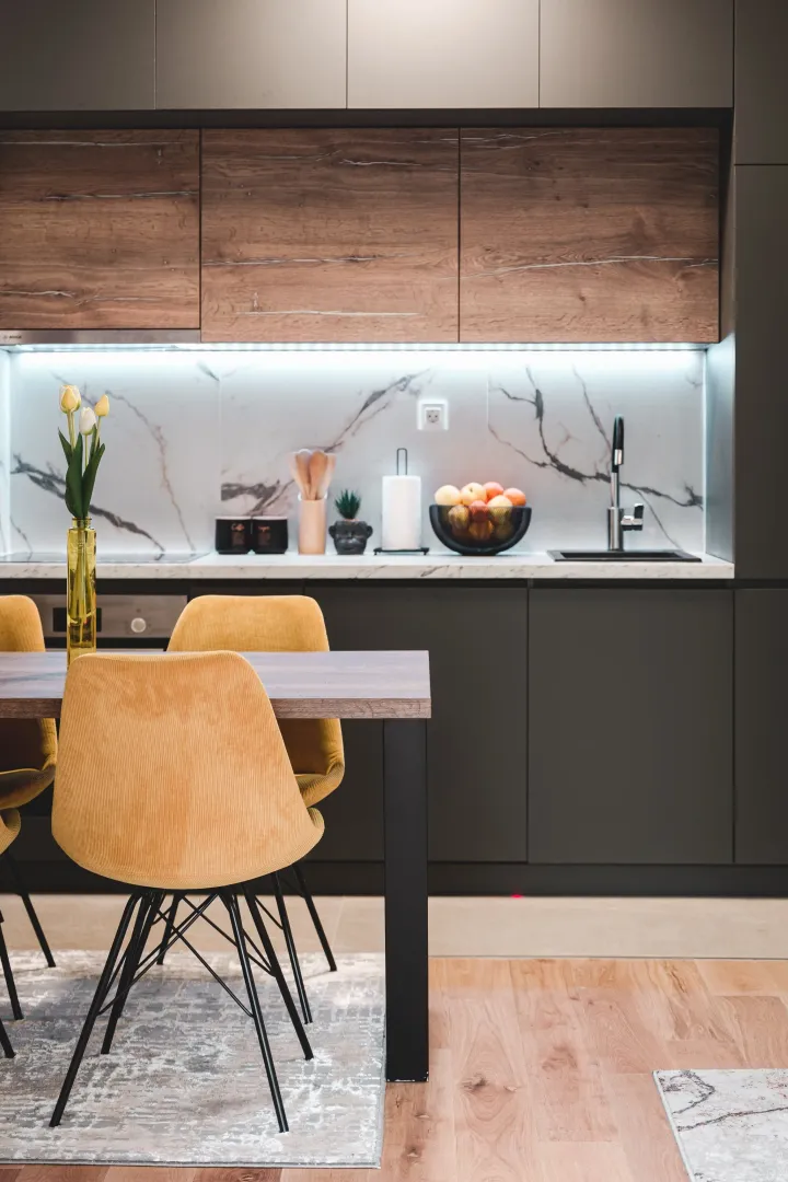 Modern kitchen with dark cabinetry, wooden accents, and a dining table with yellow chairs.