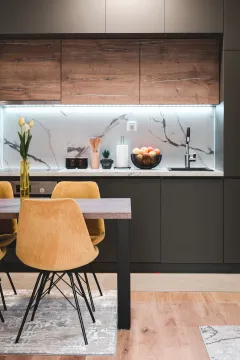 Modern kitchen with dark cabinetry, wooden accents, and a dining table with yellow chairs. - image 6
