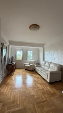 Living room with light parquet flooring, a white leather sofa set, and two windows. - image 10