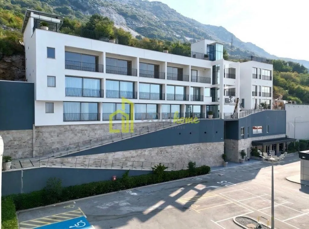 Exterior view of a modern residential building with a parking lot and mountain landscape in the background.