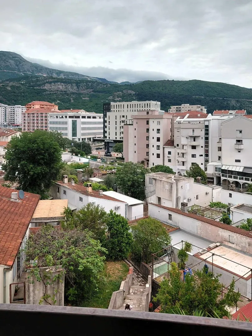 Pogled sa prozora na gradski krajolik i okolne planine.