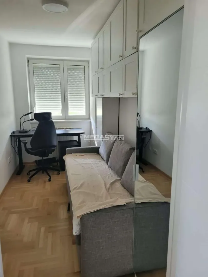 Manja spavaća soba sa krevetom, radnim stolom i ugradnim ormanom.