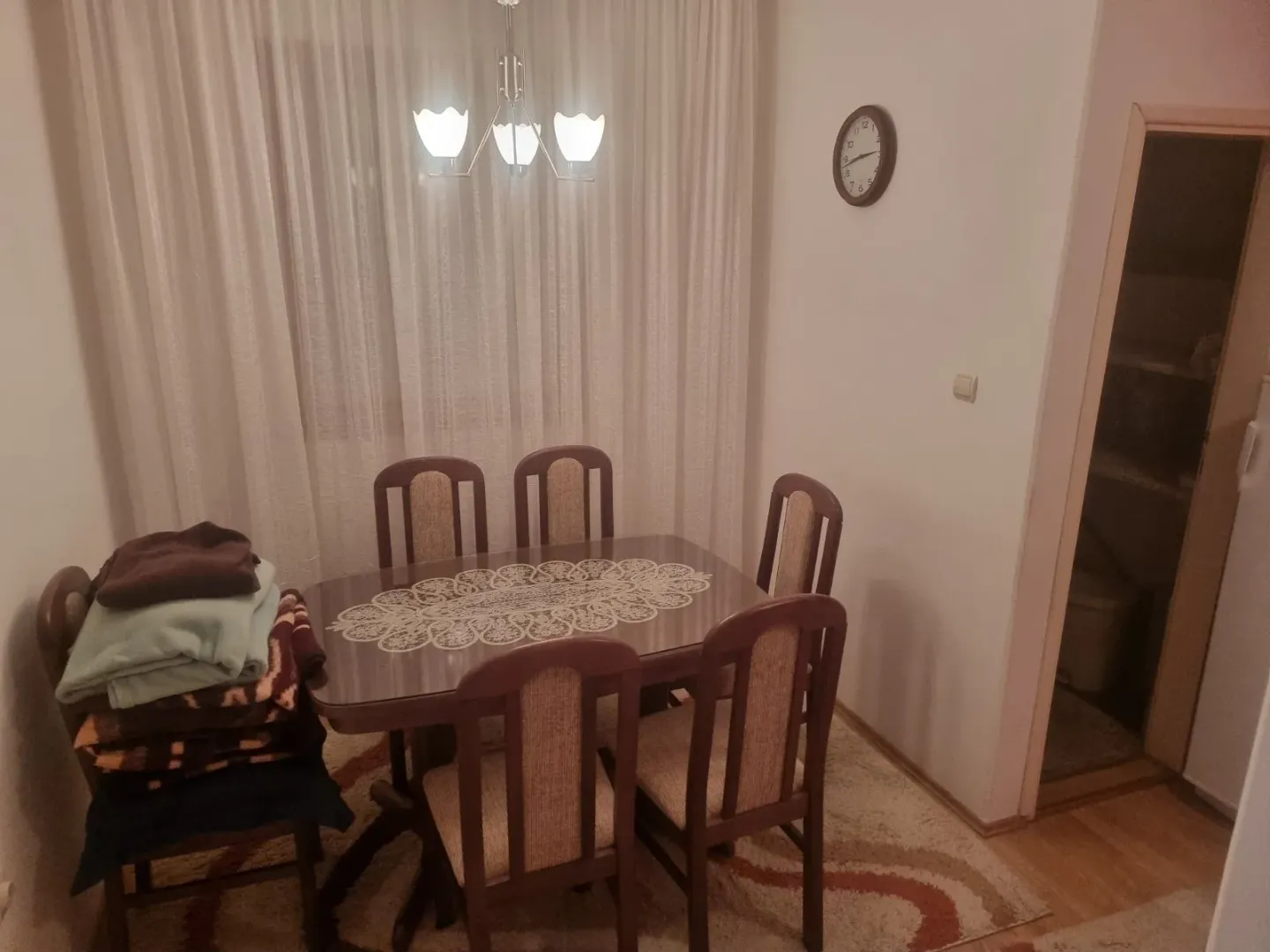 Trpezarija sa stolom, stolicama i složenim ćebadima na jednoj stolici.
