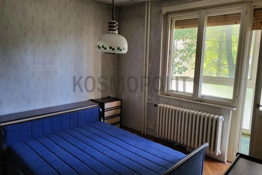 Spavaća soba sa plavim krevetom, prozorom i radijatorom.