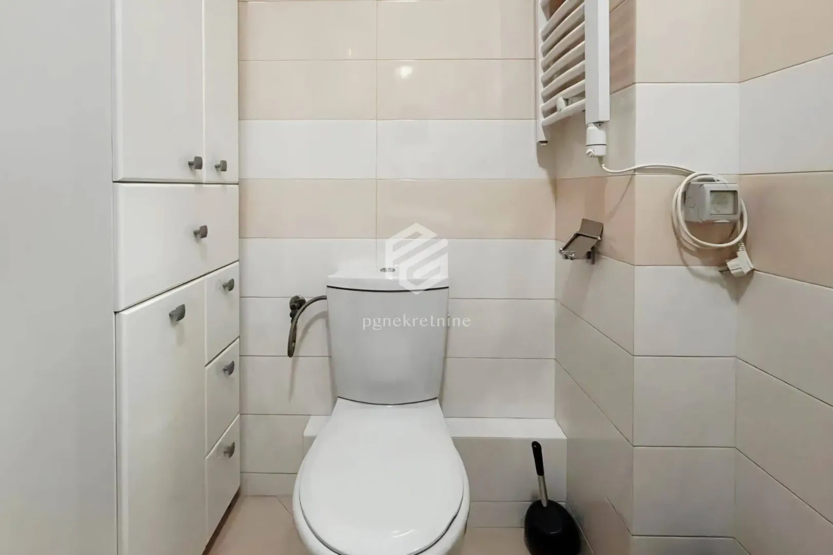 Bathroom with toilet, built-in cabinets, and light-toned ceramic tiles.