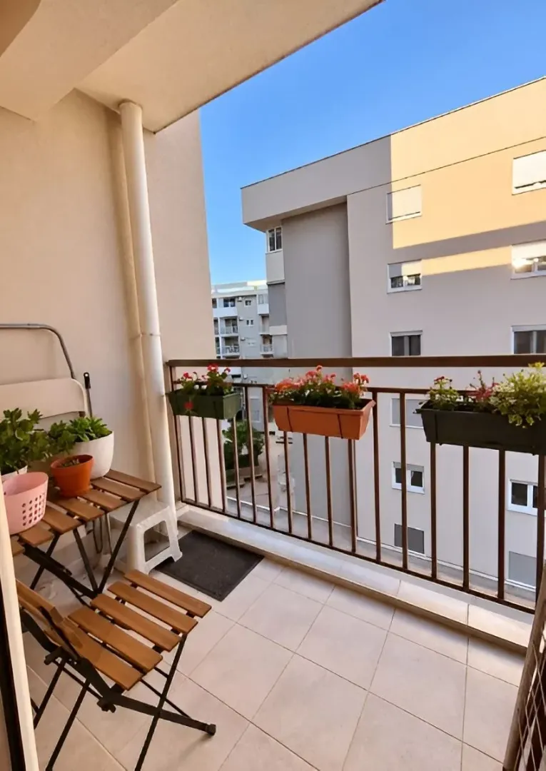 Smaller furnished balcony with a table, chairs, and flower pots.