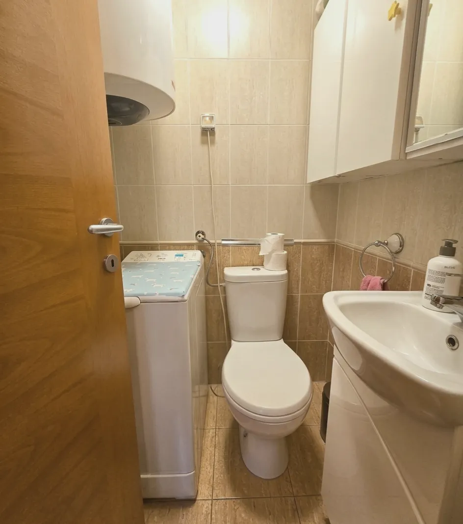 Kompaktno kupatilo sa WC šoljom, umivaonikom, veš mašinom i zidnim ormarićem.