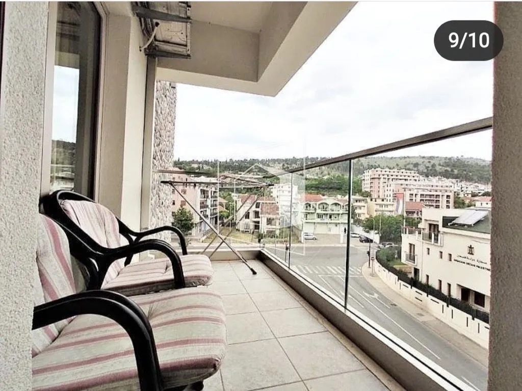 Covered balcony with seating furniture and a view of the city street and buildings.