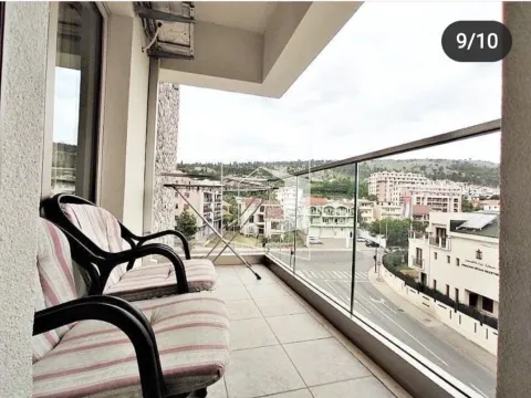 Covered balcony with seating furniture and a view of the city street and buildings. - image 8
