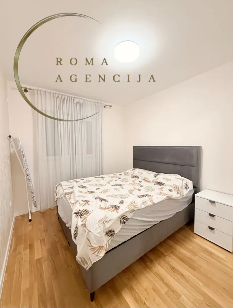 Bright bedroom with a double bed, white nightstand, and a window with curtains.