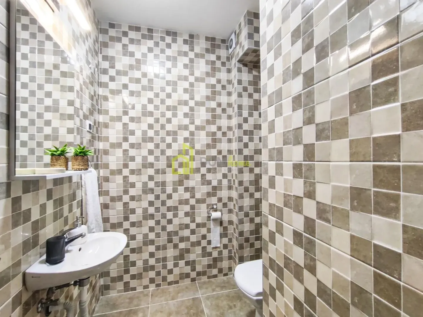 Kupatilo obloženo keramičkim pločicama sa umivaonikom i WC šoljom.