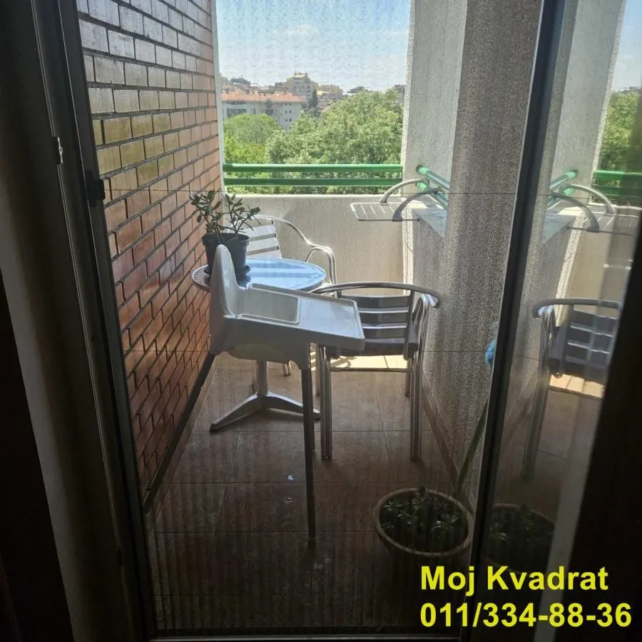 Manji namešten balkon sa stolom, stolicama i pogledom na zelenilo.