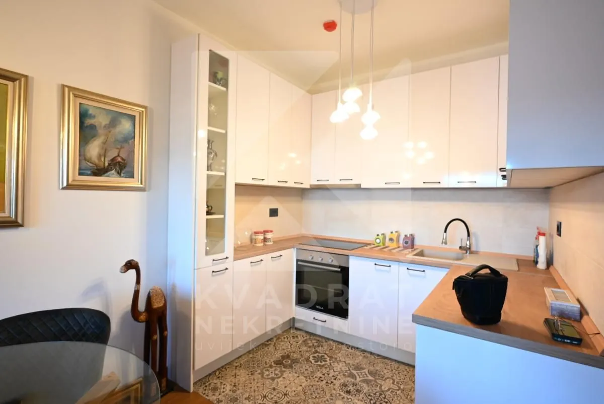 Moderna bijela kuhinja sa ugradnim aparatima i trpezarijskim dijelom.