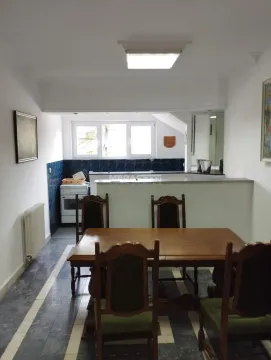 Trpezarija sa drvenim stolom i stolicama i pogledom na kuhinju u pozadini. - image 9