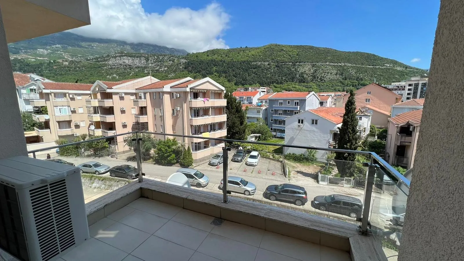 Pogled sa terase na okolne zgrade i planine u pozadini.