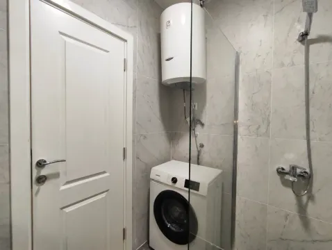 Modern bathroom with a glass shower enclosure, water heater, and washing machine. - image 3
