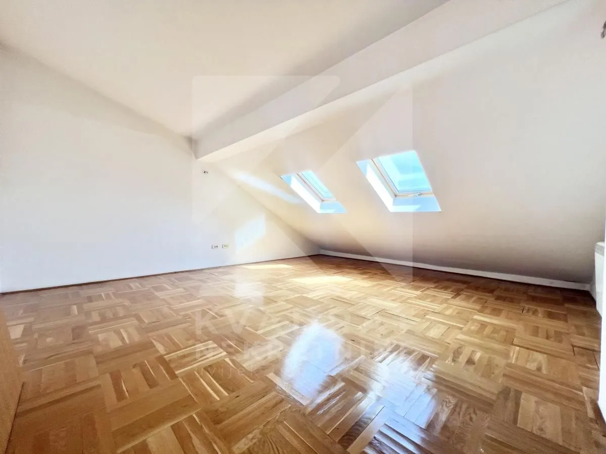 Empty attic room with parquet flooring and skylights.