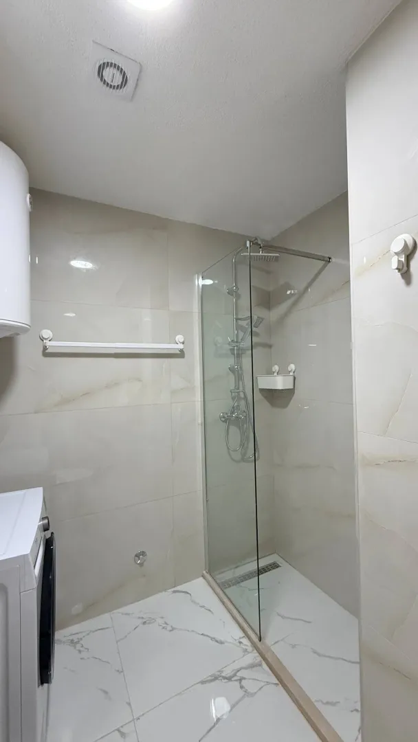 Moderne kupatilo sa tuš kabinom obloženo svijetlim pločicama.