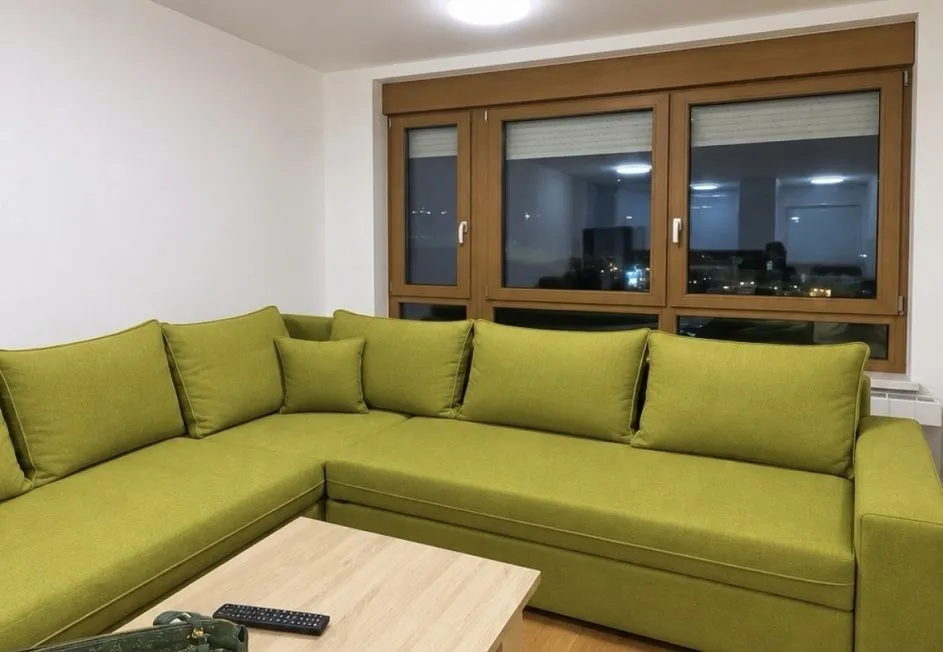 Living room with a large green sectional sofa and wooden windows.