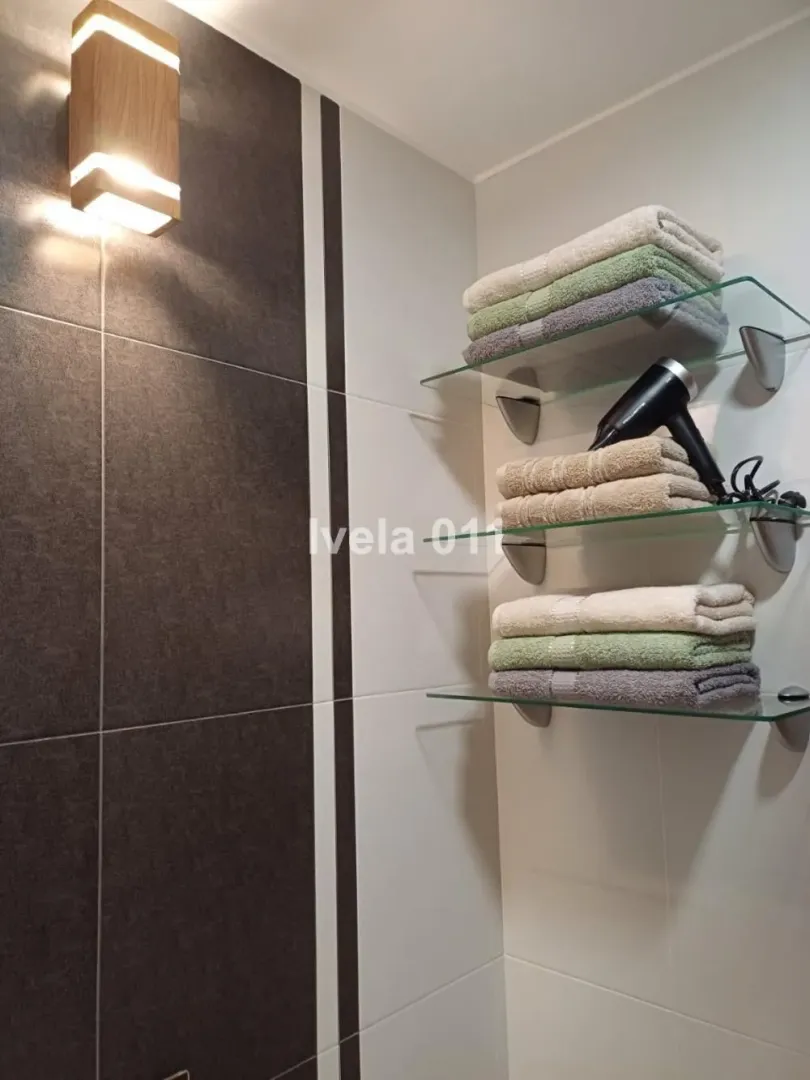 Bathroom with glass shelves holding towels and a hair dryer.