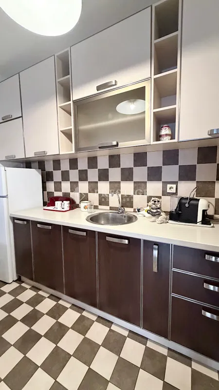 Moderna kuhinja sa bijelim i tamnim elementima i šahovskim pločicama.