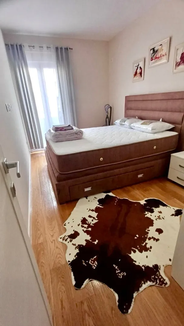 Namještena spavaća soba sa bračnim krevetom, prozorom i parketom na podu.