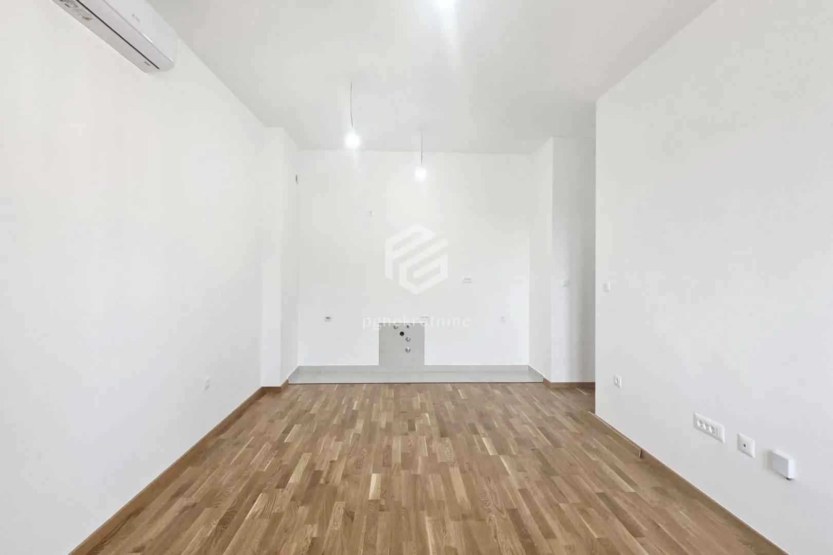 Prazna soba sa bijelim zidovima i drvenim podom.