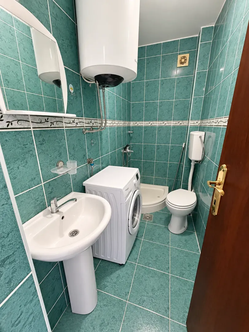 Small bathroom tiled in green with a washbasin, washing machine, and toilet.
