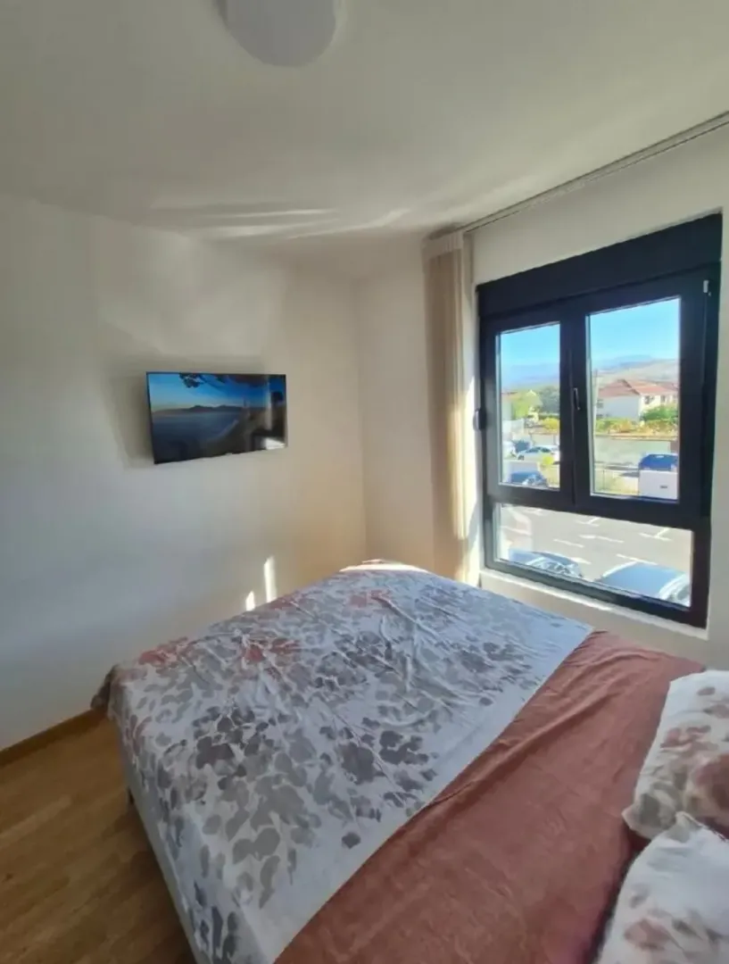 Svjetla spavaća soba sa bračnim krevetom, televizorom na zidu i prozorom sa pogledom na okolinu.