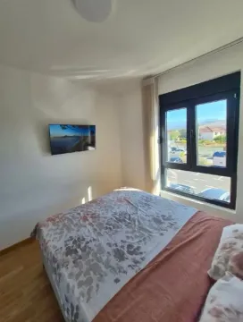 Svjetla spavaća soba sa bračnim krevetom, televizorom na zidu i prozorom sa pogledom na okolinu. - image 6