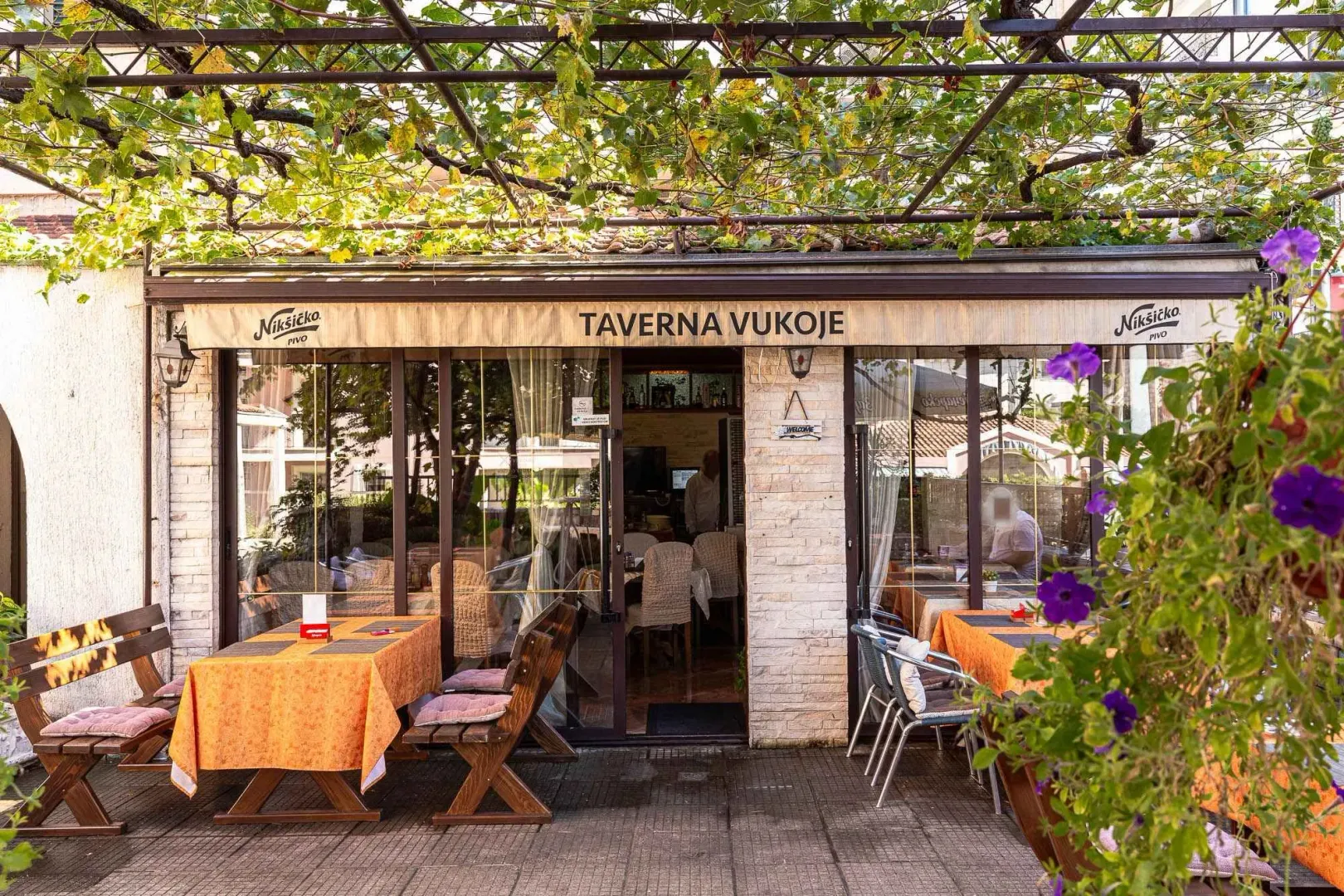 Charming outdoor restaurant terrace with tables under a grapevine trellis.
