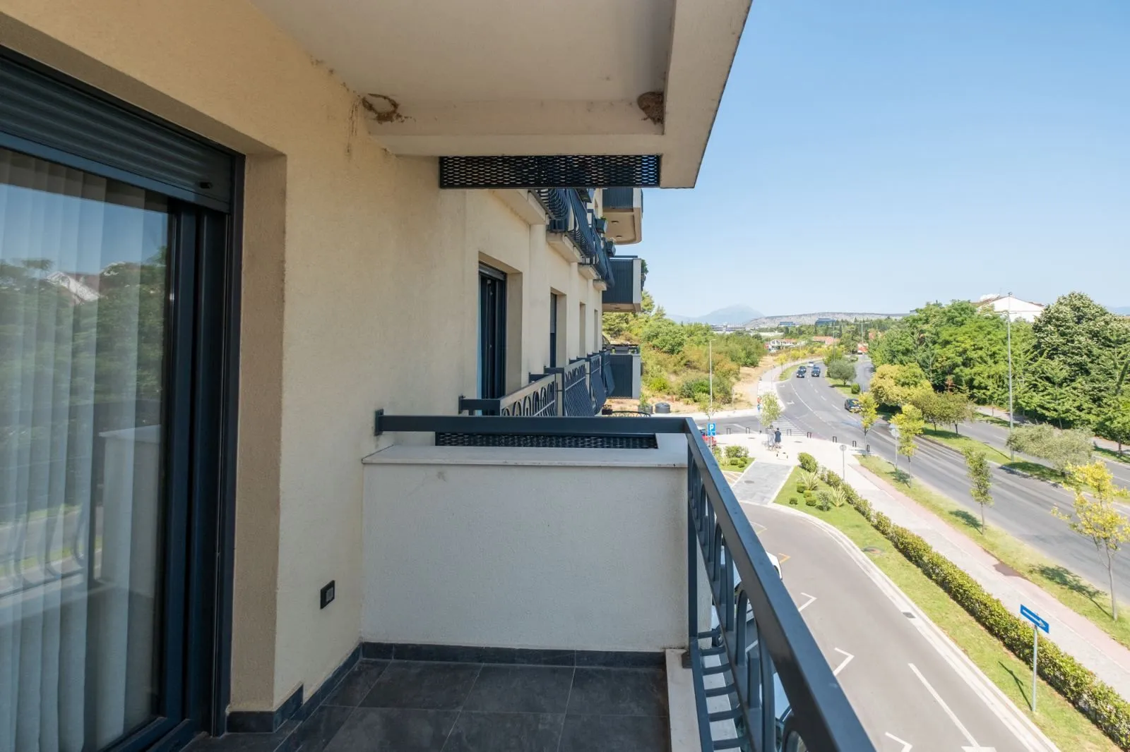 Balkon sa pogledom na ulicu i okolno zelenilo.