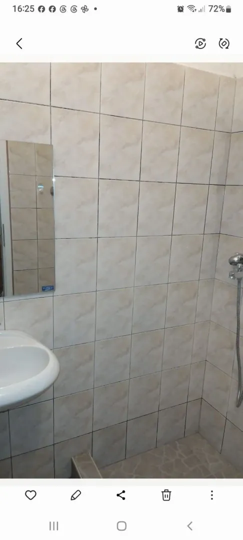 Manje kupatilo sa tuš kabinom, umivaonikom i ogledalom obloženo keramičkim pločicama.