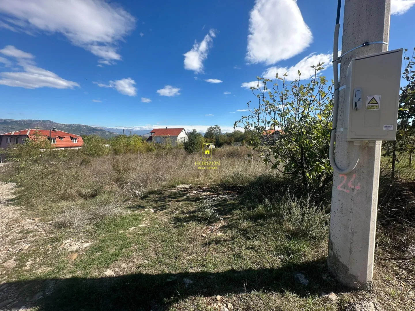Pogled na plac i okolne kuće sa stubom za struju u prvom planu.