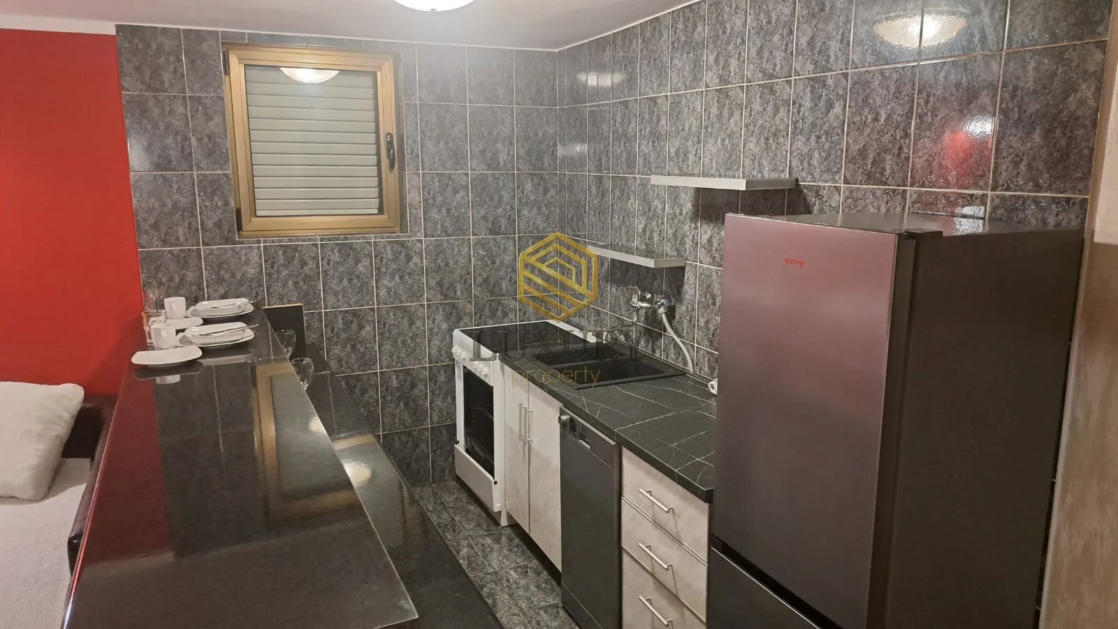 Manja opremljena kuhinja sa šankom i sivim keramičkim pločicama.
