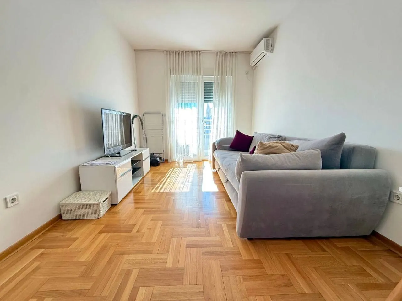 Living room with a sofa, TV, and parquet flooring.