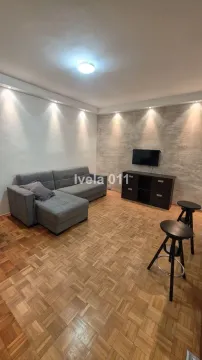 Dnevna soba sa sivom ugaonom garniturom, TV-om i parketom na podu. - image 3