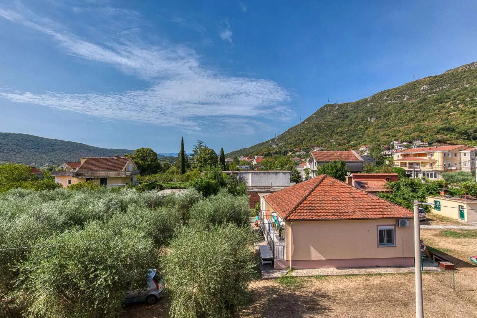 Pogled sa terase na naselje, okolno zelenilo i brda u pozadini.