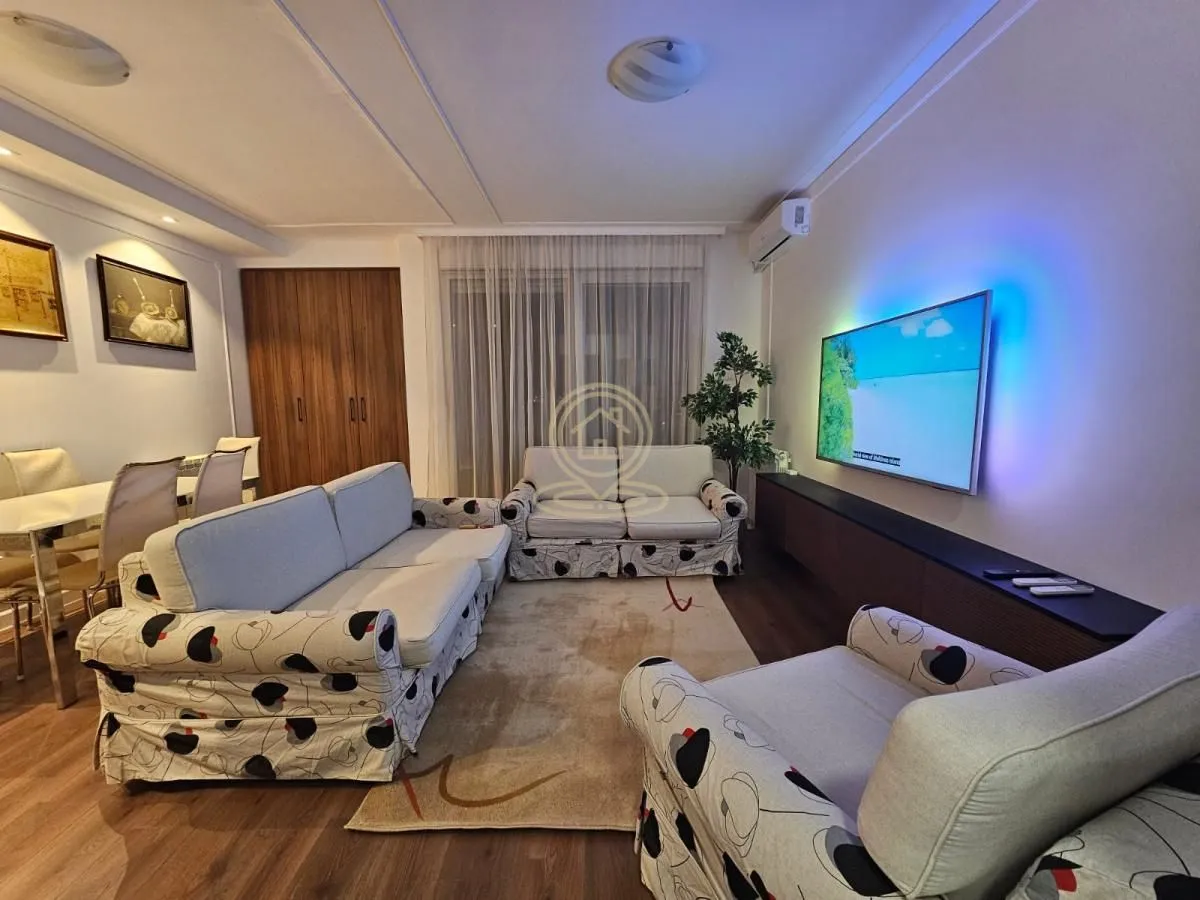 Living room with a sofa set, TV, and a dining area in the background.