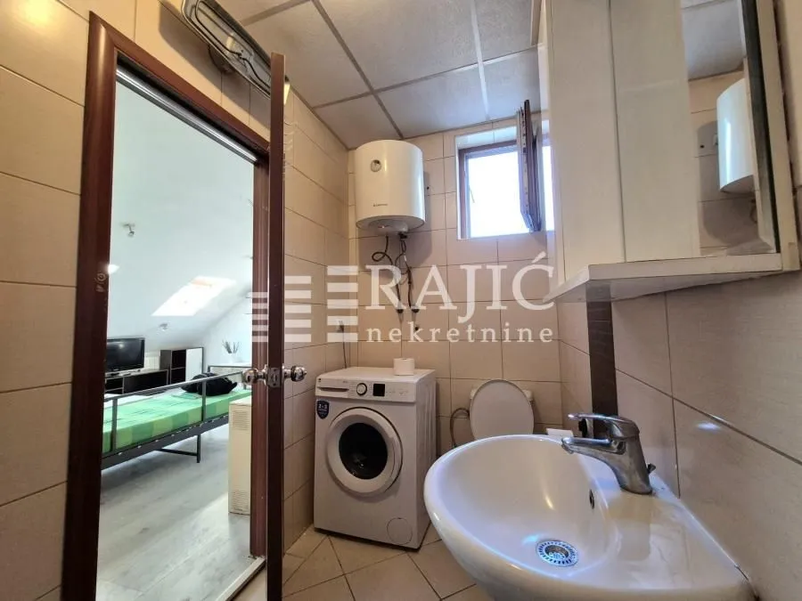Small bathroom with a washbasin, washing machine, and water heater, with a view into the bedroom.