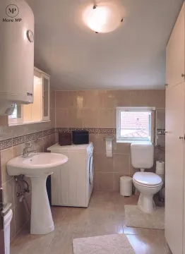 Kupatilo opremljeno umivaonikom, WC šoljom, mašinom za veš i zidnim pločicama. - image 7