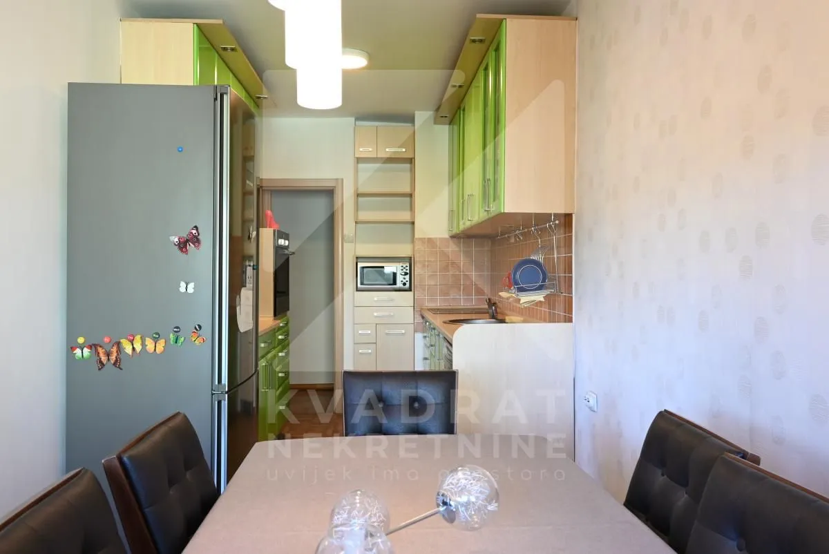 Long kitchen with green cabinets and a dining table in the foreground.