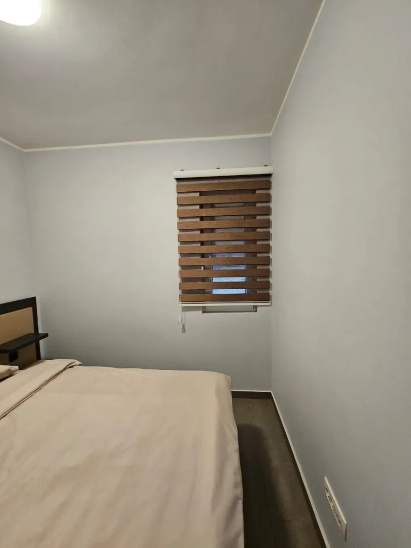 Uređena spavaća soba sa bračnim krevetom i prozorom sa roletnama.