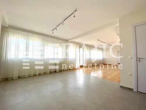 Spacious bright living room with large windows and parquet flooring.