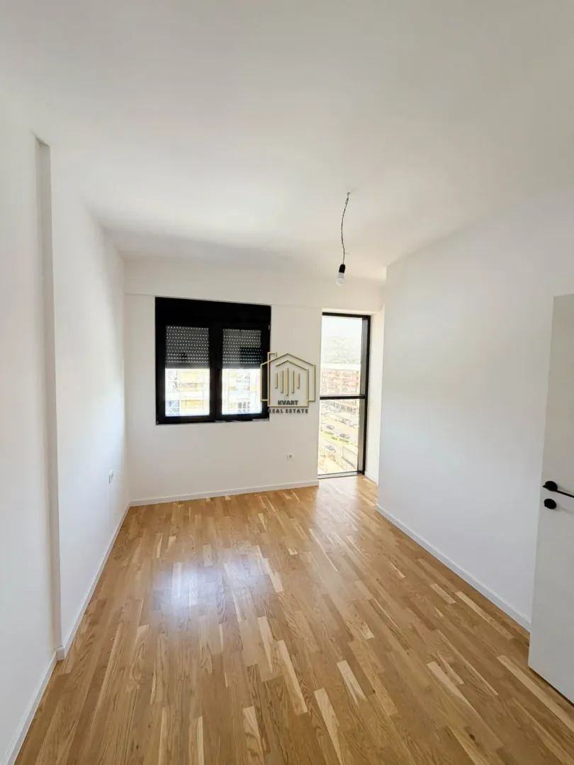 Empty room with white walls, wooden flooring, a window, and a balcony door.