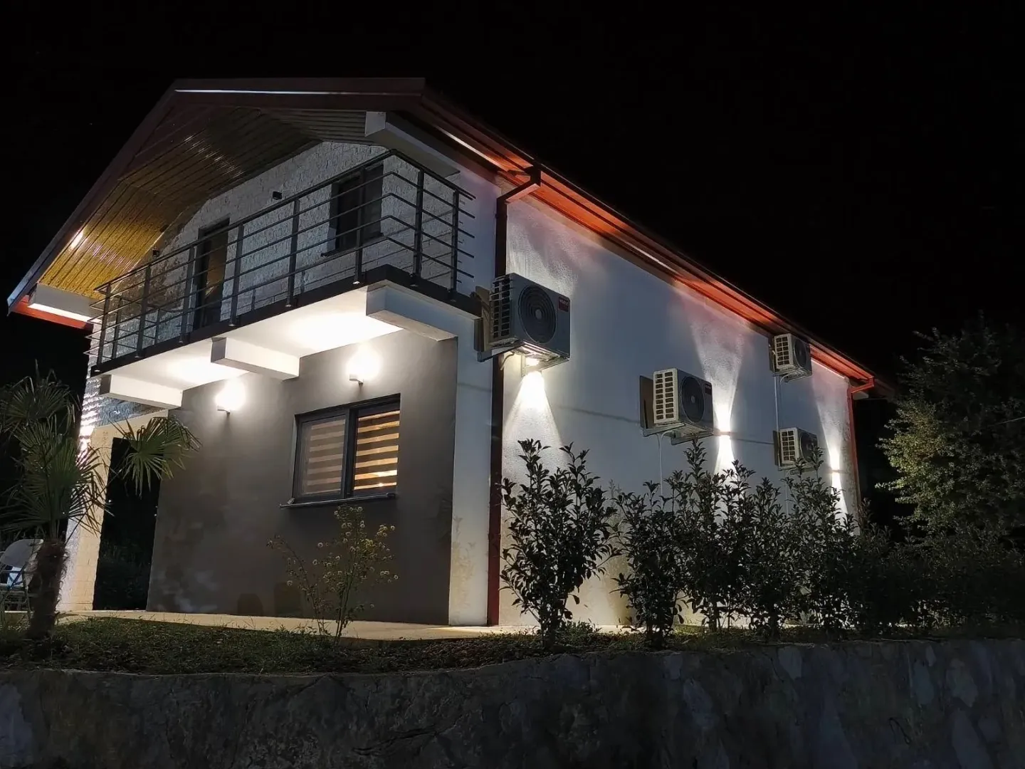 Night view of the house with an illuminated facade, balcony, and installed air conditioning units.