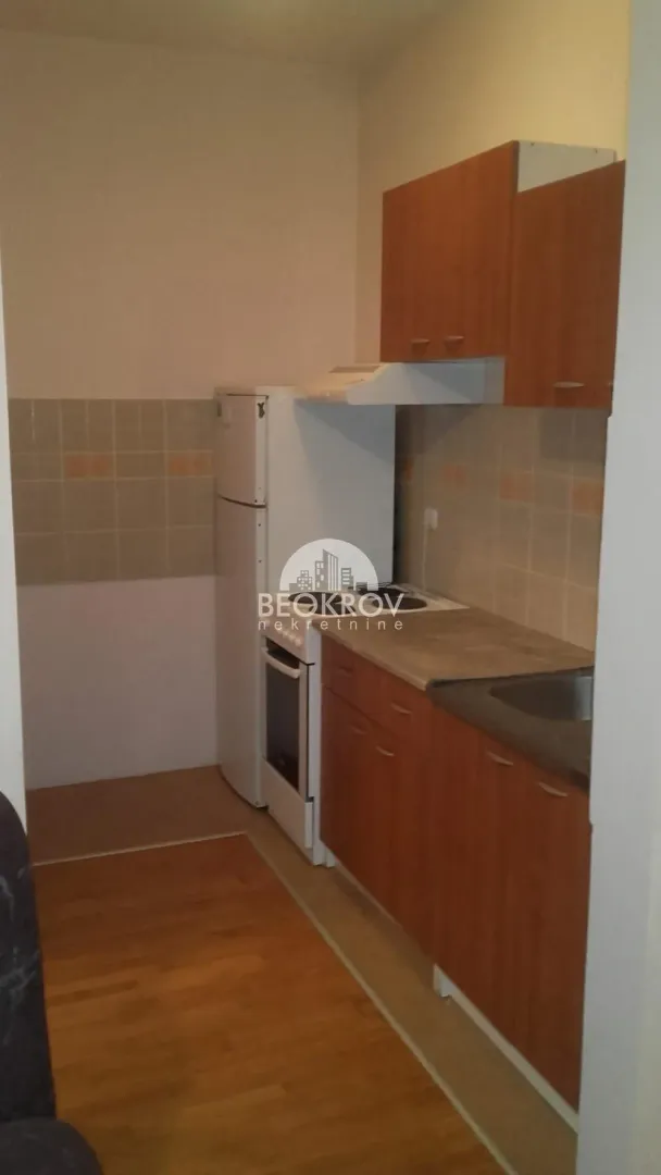 Manja kuhinja sa drvenim elementima i ugrađenim kućnim aparatima.