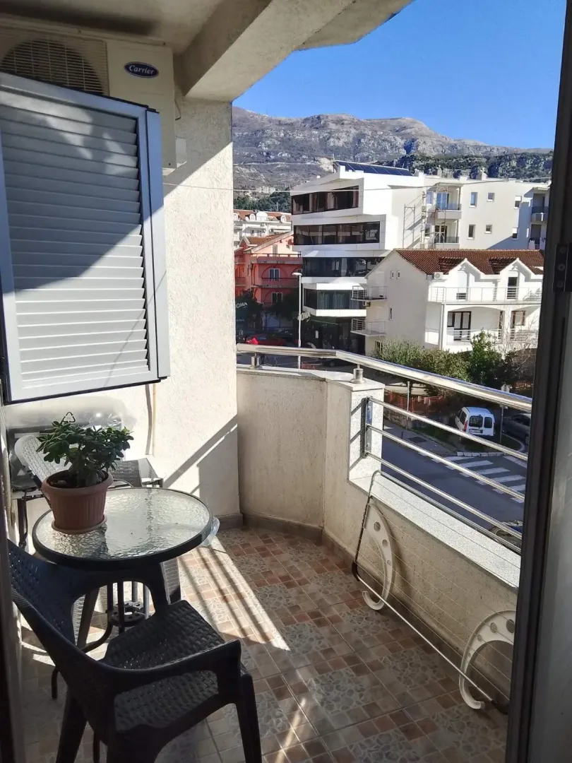 Namješten balkon sa stolom, stolicama i pogledom na okolne zgrade i brda.