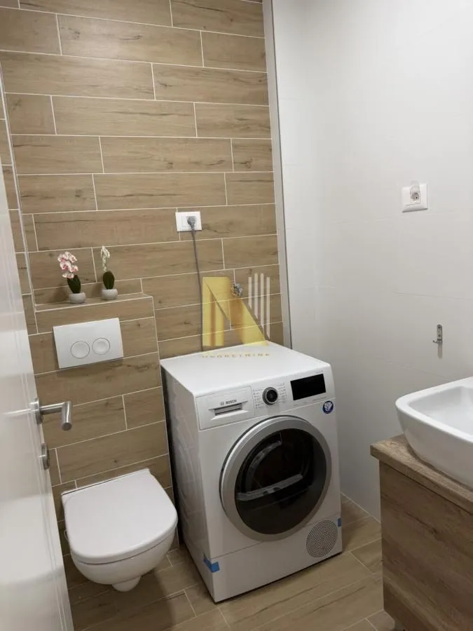 Moderno opremljeno kupatilo sa veš mašinom i belim sanitarijama.