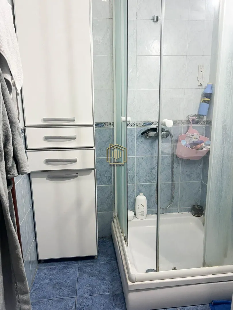 Manje kupatilo sa tuš kabinom i bijelim ormarićem.